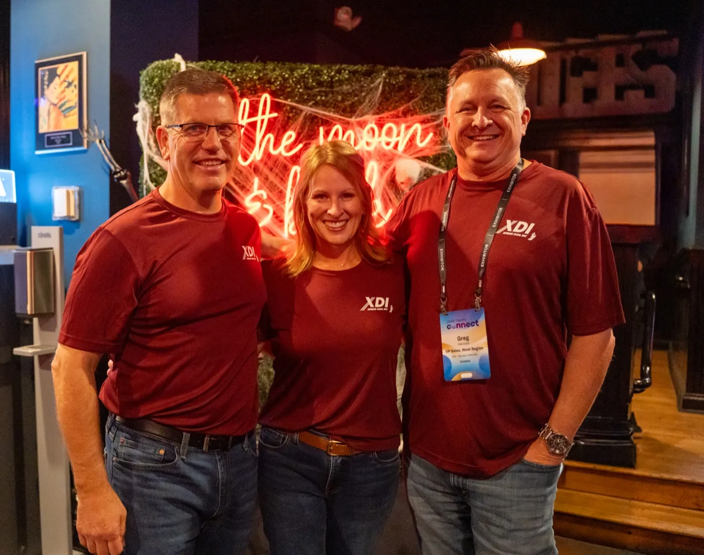 Kansas City corporate event photographer - three hosts in matching maroon company shirts under a neon sign