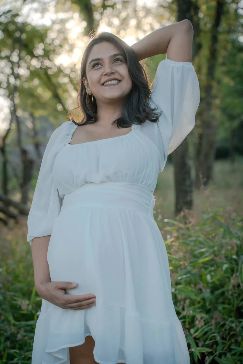 Kansas City maternity photographer - expecting mother in a white dress smiling in a sunlit forest