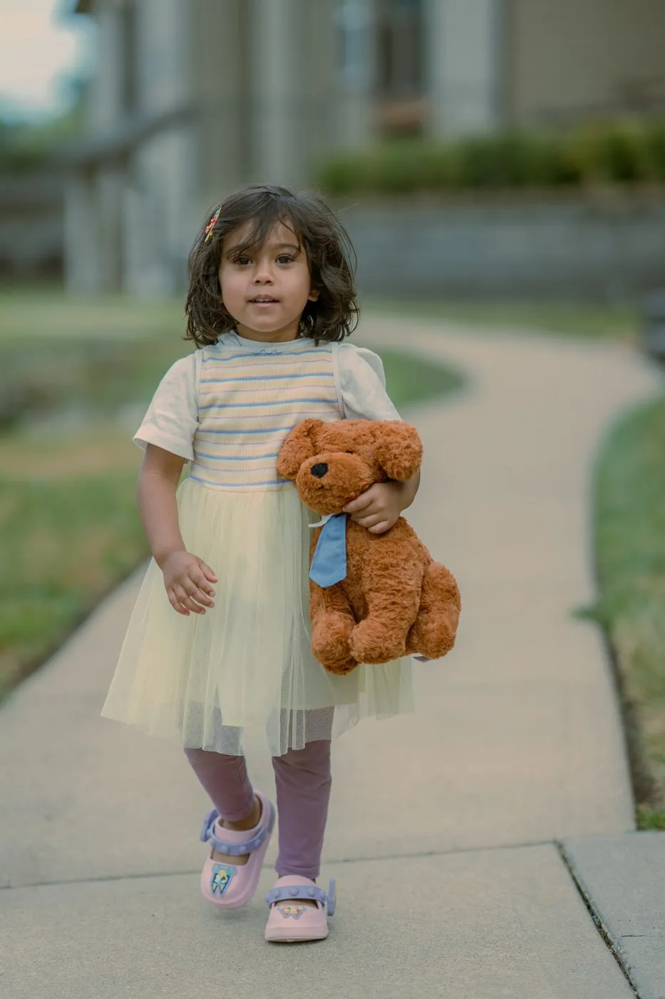 Kansas City family photographer - toddler walking along a sidewalk carrying her teddy bear